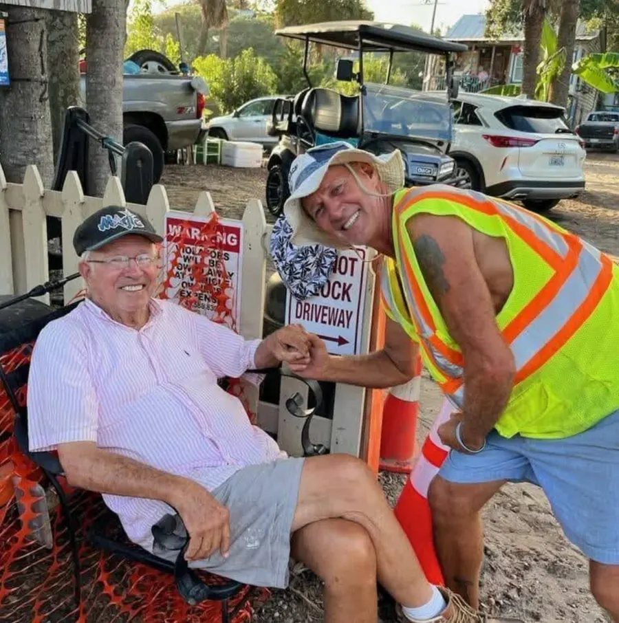 Dagwood in a striped shirt and ball cap, sitting in his chair by the lot entrance and fist-bumping Andy