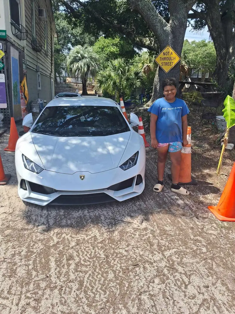 A white Lamborghini parked on the sand at the lot with Tara standing beside it