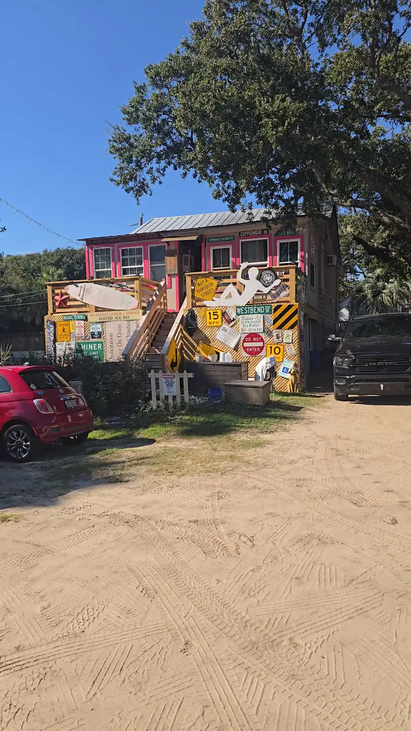 The sand lot under the live oaks with the pink house behind it