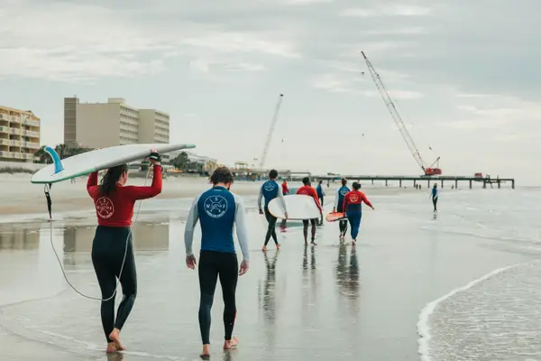 Surfers in wetsuits carrying boards down the beach toward the pier